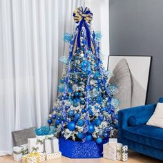 a blue christmas tree in a living room with presents on the floor next to it