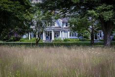 a large white house sitting in the middle of a lush green field next to trees