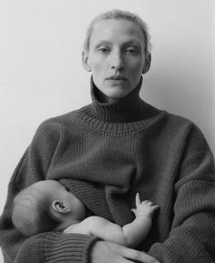 a black and white photo of a woman holding a baby in her arms while wearing a turtle neck sweater