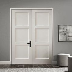 an empty room with two white doors on the wall and a round ottoman next to it