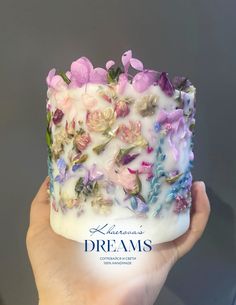 a hand holding up a cake with flowers on it's icing and frosting