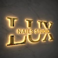 the logo for nails studio is lit up in gold on a white wall with marble