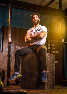 a man sitting on top of a wooden box in a crossfit gym with his arms crossed