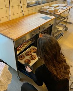 a woman is looking into an oven with doughnuts in the baking area behind her