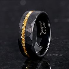 a black and gold wedding ring with yellow glitter inlaying the center, on a dark background