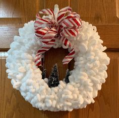 a white wreath with red and white striped ribbon hanging on the front door, decorated with small christmas trees