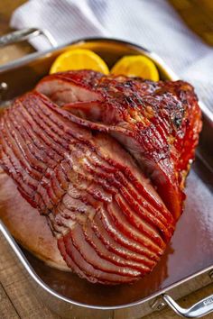 a large piece of meat sitting on top of a pan next to sliced lemons