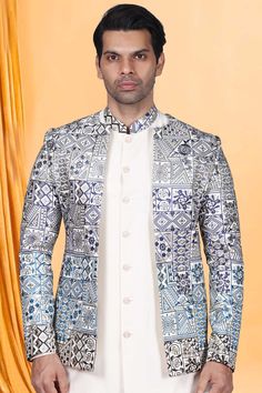 a man standing in front of a yellow curtain wearing a white shirt and jacket with blue patterns on it