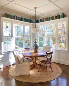 a dining room table and chairs with bookshelves on the wall behind them in front of large windows