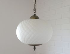 a white ball hanging from a chain on a light fixture in front of a brick wall