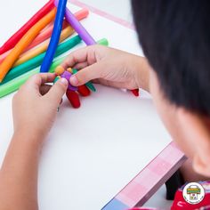 a child is playing with colored crayons on a white table in front of them