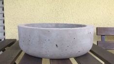 a concrete bowl sitting on top of a wooden table next to a wall and bench