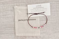 a small bracelet with pink and white beads sits on top of a cloth bag next to a card that says love