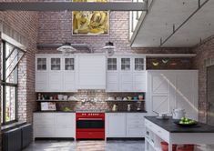 a kitchen with white cabinets and red stove top oven next to an open floor plan