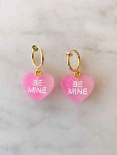 Obsessed is an understatement! Pay homage to your favorite Valentine's Day candies with these adorable be mine huggies. Available in both pierced hoops or clip on styles (for those without their ears pierced) these earrings are super fun and eye catching. Choose from a matte candy heart in a number of different colors or a two color glitter heart. The perfect size they are noticeable without being overwhelming. The charms are lightweight and easy to wear. Hoops are gold plated and nickel free. M Cute Pink Hoop Earrings For Valentine's Day, Pink Hoop Earrings For Valentine's Day, Pink Heart Huggie Earrings For Valentine's Day, Pink Huggie Heart Earrings For Valentine's Day, Pink Heart Charm Hoop Earrings For Valentine's Day, Pink Hoop Earrings With Heart Charm For Valentine's Day, Pink Huggie Heart Earrings As Gift, Cute Dangle Hoop Earrings For Valentine's Day, Cute Huggie Hoop Earrings For Valentine's Day