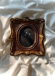 an old clock is sitting on a white sheet with gold trimmings and ornate frame