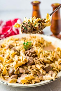 a spoon full of pasta with meat and parmesan cheese on the side, being held up by a fork