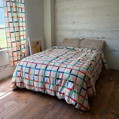 a bed sitting on top of a wooden floor next to a window with colorful curtains