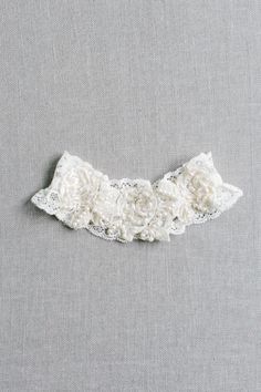 a white lace collar with flowers on it's side, against a gray background