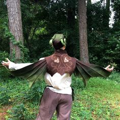 a man dressed as a dragon standing in the woods with his arms spread out wide