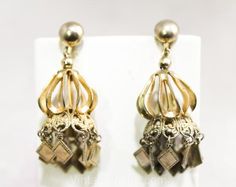 Flirty chandelier earrings with lots of movement!  They're two dangling layers of fluted metal and filigree, ending in fluttering diamond shaped accents.  Measurements  Each 2 3/8 x 7/8 Inches   Era  1960s   Label   None, factory made   Materials  Brassy goldtone metal   Closure  Screwbacks  Condition  Excellent  Condition Detail  Shows light regular wear as the finish has a more muted gold hue in a few areas, hard to notice unless closely scrutinized  Additional photos are often available.   Qu Belly Dancer, Hollywood Regency Style, Belly Dancers, Diamond Shaped, Hollywood Regency, Chandelier Earrings, Boho Bohemian, Diamond Shapes, 1960s