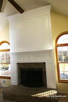 an empty living room with a fireplace and two windows in the corner, all painted white