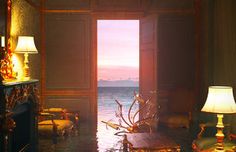 a living room with an open door leading to the ocean at sunset or sunrise time