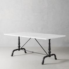 a white table sitting on top of a gray floor next to a wall with black legs