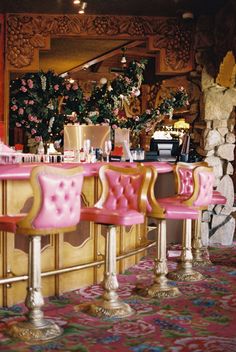 four pink chairs sitting at a bar in front of a wall with flowers on it