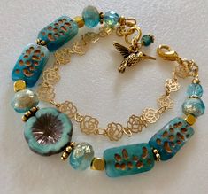 Lovely double strand beaded Premium Czech glass flower bracelet featuring table cut matte aqua with bronze rectangular beads, gold etched ivory/aqua rondelles, fire polished aqua Aurora Borealis crystals, and single 14 mm turquoise Picasso pansy flower. All accented with antique gold plated daisies and shiny gold cubes. Satin Hamilton rose chain adds the perfect delicate second strand. Premium gold electroplated brass chain in satin finish with intricate rose flower pattern. Bracelet is beaded o Unique Gold Beaded Bracelets Nickel-free, Unique Gold Beaded Bracelets Nickel Free, Elegant Turquoise Czech Glass Beaded Bracelets, Elegant Gold Czech Glass Bracelets, Elegant Gold Bracelets With Czech Glass, Paris Charm Bracelet, Rose Flower Pattern, Pattern Bracelet, Pansy Flower