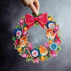 a hand holding a christmas wreath decorated with deers and flowers on a gray background