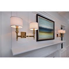 a painting hangs on the wall above a mantle with two lamps and a framed art piece