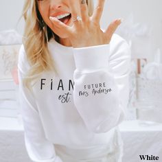 a woman is holding her hand up to the camera while wearing a white sweatshirt with writing on it