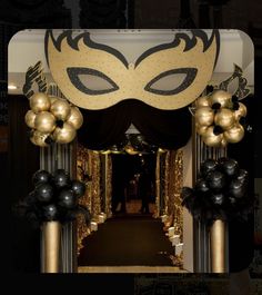 an entrance decorated with black and gold balls, balloons and a masquerade mask