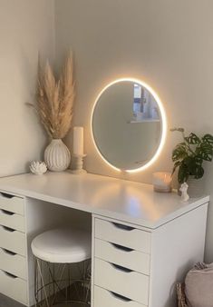 a white desk with a round mirror on it and some plants in front of it