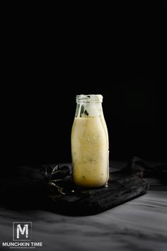 a glass jar filled with liquid sitting on top of a wooden tray next to a black background