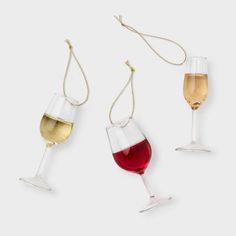 three wine glasses with different colored liquids in them on a white surface, one is empty and the other has a chain attached to it