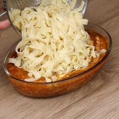 someone is grating pasta into a casserole in a glass dish on a wooden table