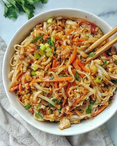 a white bowl filled with noodles, carrots and other vegetables next to chopsticks