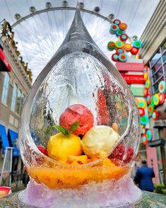 a glass bowl filled with different types of fruits and vegetables in front of a ferris wheel