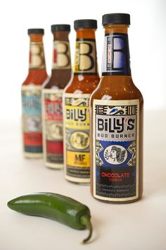 hot sauce bottles lined up next to a green pepper