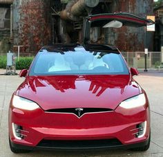 a red tesla car parked in front of an old factory with its hood up and the door open