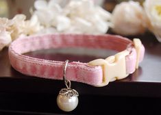 a pink dog collar with a pearl charm on it's side and flowers in the background