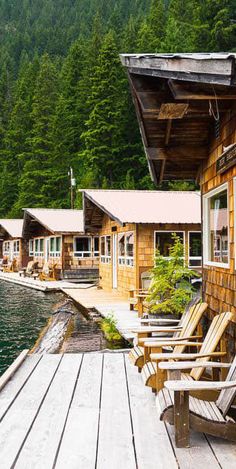 a wooden dock with chairs on it next to some buildings and trees in the background