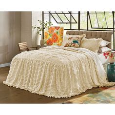 a bed with white ruffled bedspread, pillows and blankets on top of it