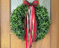 a green wreath with red, yellow and black ribbons hanging on the front door