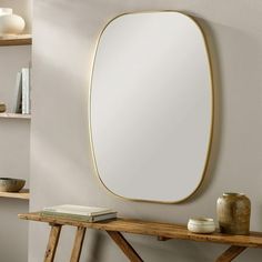 a mirror sitting on top of a wooden table next to a book shelf and vase