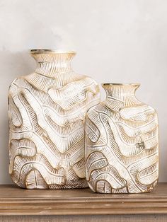 two white vases sitting on top of a wooden shelf