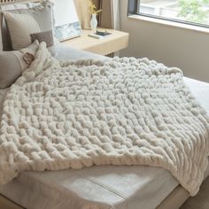 a bed with a white blanket on top of it next to a night stand and window