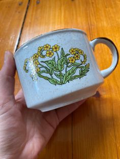 a hand holding a white coffee cup with yellow flowers on it